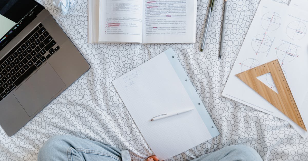 Flat lay of a study area with an open laptop, books, notes, and stationery on a bed.