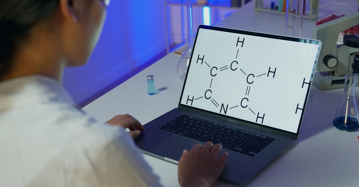A scientist reviews a chemical formula on a laptop in a laboratory setting.